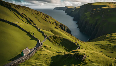 A picturesque landscape with winding road, coastal cliffs and a small house. The lush green grass slopes down to the ocean, creating a serene and peaceful atmosphere.の写真素材