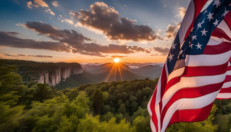 An American flag waves in the wind against a backdrop of a breathtaking sunset over a mountain range. The golden rays of the setting sun illuminate the clouds, casting a warm glow on the landscape. The flag, a symbol of freedom and patriotism, stands tall and proud, representing the beauty and strength of the nation.の写真素材