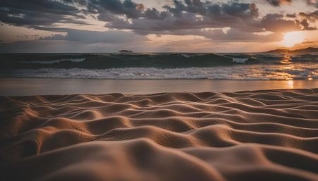 Close-up of sand dunes on a beach with a stunning sunset in the background. The warm glow of the sun illuminates the waves and the sky.の写真素材