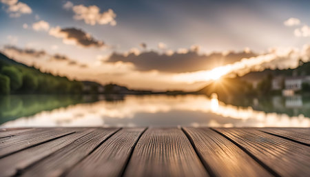 A close-up shot of a wooden dock overlooking a calm lake at sunset. The sky is ablaze with golden...