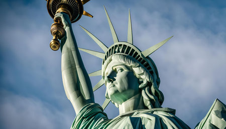A close-up portrait of the Statue of Liberty, showing her majestic face and the iconic torch she holds high. The green copper statue stands tall against a bright blue sky, radiating hope and freedom.の写真素材