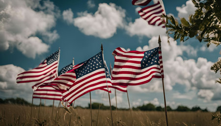 Multiple American flags waving in the wind against a backdrop of a bright blue sky with white...