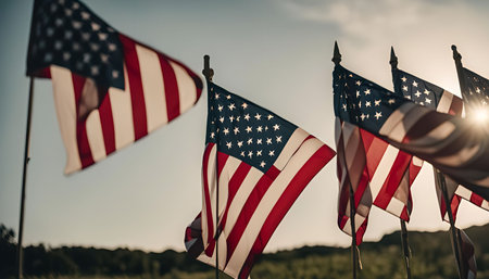 Five American flags waving in the wind against a blue sky and sunset.