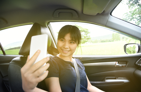 Woman taking a photo with smart phone in car with sunlight,Woman selfie in carの写真素材