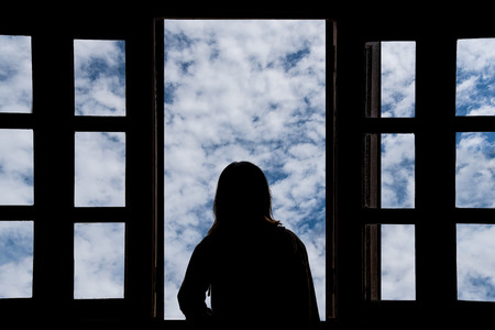 Silhouette young woman in the hotel, looking blue sky through the windowの写真素材