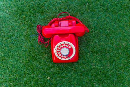 Old red phone  on the field of green grass, close up of communication vintage styeの写真素材