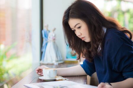 Asian student woman relaxing with hot coffee and Magazine at cafe, Young  business woman