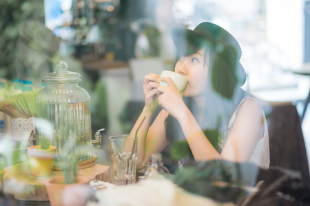 Hipster asian woman drinking coffee in cafe through mirrorの写真素材