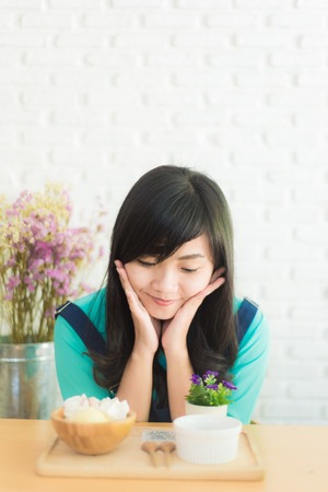 Asian woman having cup of coffee and icecream cake in cafe with white brick wall backgroundの写真素材