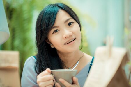 Business asian woman holding coffee cup in coffee shop smile and looking to cameraの写真素材