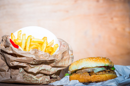Closeup of burgers  served with French Fries on crumpled brown paper and rustic wood tableの写真素材