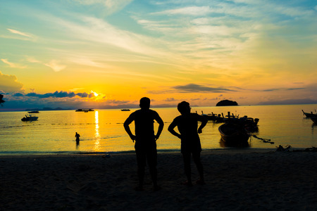 Silhouettes of young couple of people on beach at the sunrise timeの写真素材