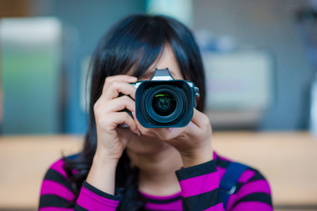 Asian woman with camera sitting in coffee shopの写真素材