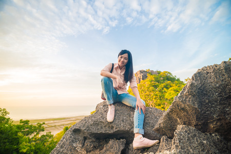 Asian hiker woman with backpack relaxing on top of a mountain and enjoying valley view during sunriseの写真素材