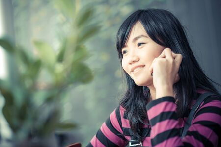 Beautiful asian young woman speaking by mobile phone and smiling in coffee shopの写真素材
