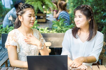 Two asian young female friends use internet together on laptop outdoorの写真素材