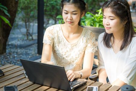 Two asian young female friends use internet together on laptop outdoorの写真素材