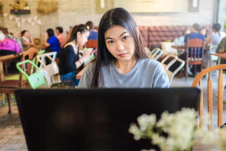 Beautiful young asian woman with coffee using laptop in loft style coffee shopの写真素材