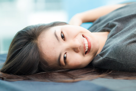 Fashion photo of beautiful young asian woman lying on the bed in condominium lodern livingの写真素材