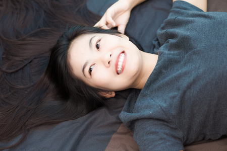 Fashion photo of beautiful young asian woman lying on the bed in condominium lodern livingの写真素材