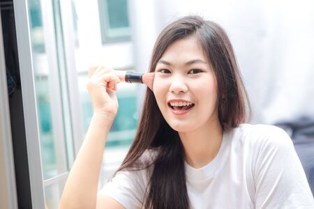 Beautiful young woman with makeup brush in living roomの写真素材