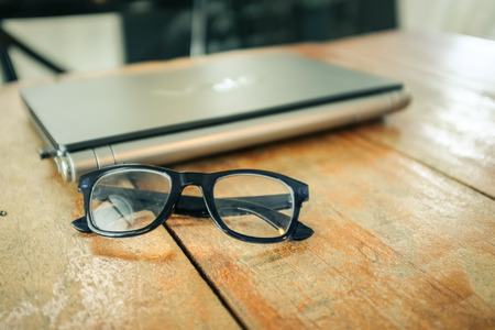 Glasses with laptop Workspace on wood table vintage filter