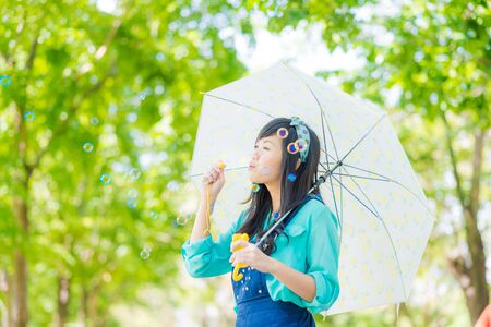 Beautiful asian young woman with green dress blowing bubble in park of cityの写真素材