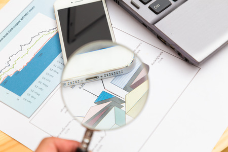 Overhead work space view of a wooden desk with electronic devices with business chart growth chartの写真素材