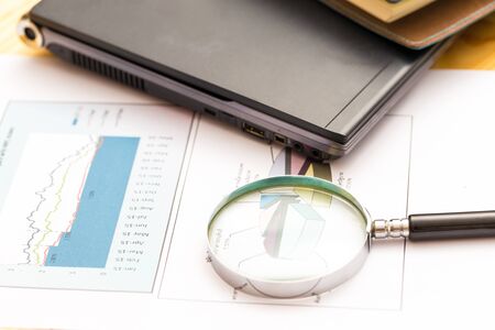 Magnifying glass to documents graphs and charts being demonstrated with laptop on tableの写真素材