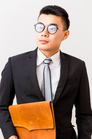 Asian smiling young business man glasses carrying a handmade leather bag on white backgroundの写真素材