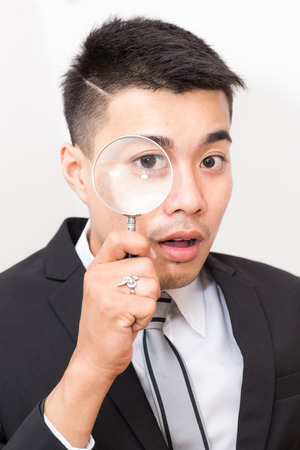 Business asian man Looking At camera Through Magnifying Glass close up on whiteの写真素材