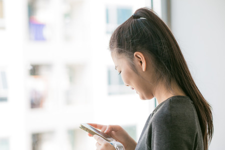 Girl texting on the smart phone in condominium living room, Asian women using smart phoneの写真素材