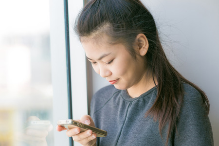 Smiling asian woman using on smartphone standing on building background.の写真素材
