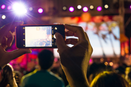 Blurred people holding their smart phones and photographing concert, concert crowd in front of bright stage lightsの写真素材