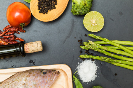 Raw fish grouper on wooden cutting board with asian spicy herb and wine on black cutting board