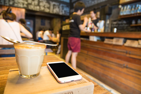Cup of lattecoffee on a wooden table with smartphone in art cafeの写真素材