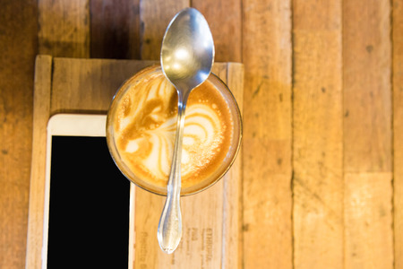 Cup of lattecoffee on a wooden table with smartphone in art cafeの写真素材