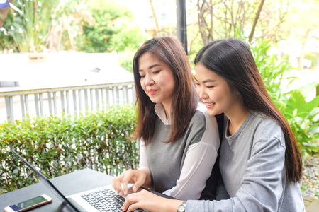 Asian woman use mobile phone and laptop for business communication in coffee shop vintage cafeの写真素材