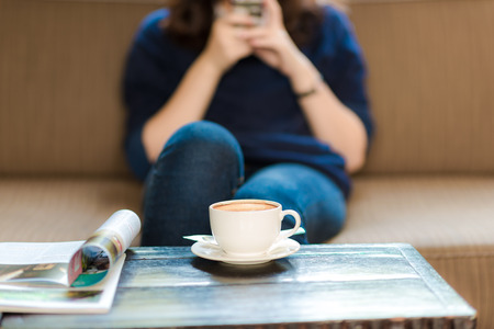 Women with cup of coffee and mobile phone on sofa in coffee shopの写真素材