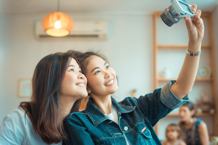 Portrait of two happy young Asian woman take selfie in cozy coffee shop, smile to cameraの写真素材