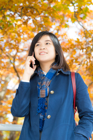 Happy young woman talking on mobile phone stand on autumn park leaf color backgroundの写真素材