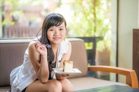 Beautiful smiling asian young woman sitting on sofa with a cakeの写真素材