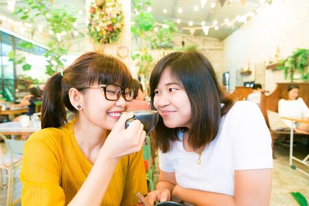 Smiling female asian friends holding coffee mugs while talking business at coffee loft store