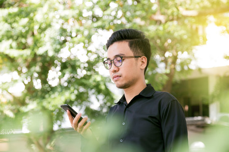 Asian man with a phone at park outdoors texting on cellphone on a sunny dayの写真素材