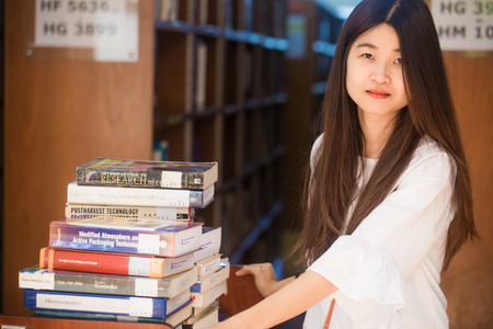 Portrait of a young attractive asian woman at the library sitting to reading a book. Education...