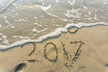 New year 2017 written on seashore sand at sunrise with waveの写真素材