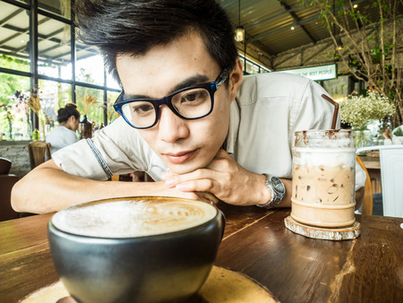 Asian student glasses man with cup of latte coffee in art cafeの写真素材