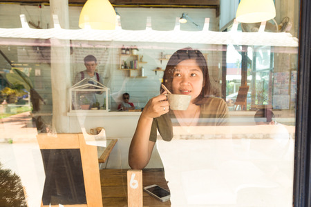 Young women drinking coffee at a cafe through mirror with cellphoneのeditorial素材