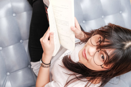 Smiling asian glasses women read book while reclining on sofa