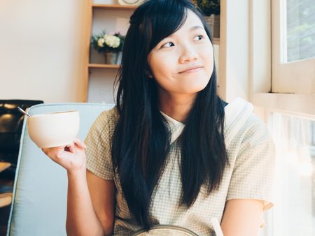 Women hold cup of latte coffee sitting on sofa in vintage modern loft cafeの写真素材
